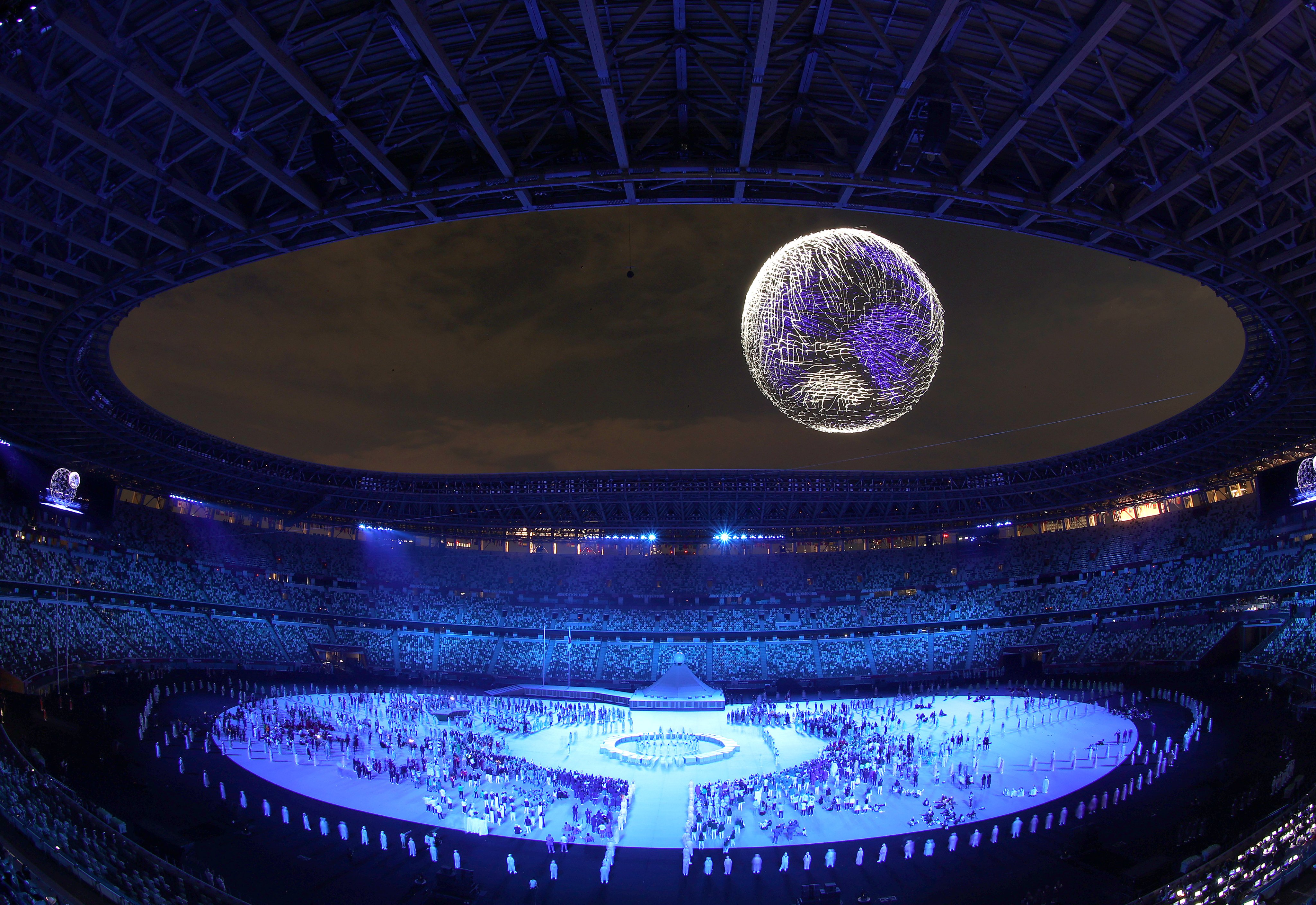 Fotografia da abertura dos Jogos Olímpicos em Tóquio mostra projeção gráfica do planeta Terra em pleno ar, no meio de um estádio.