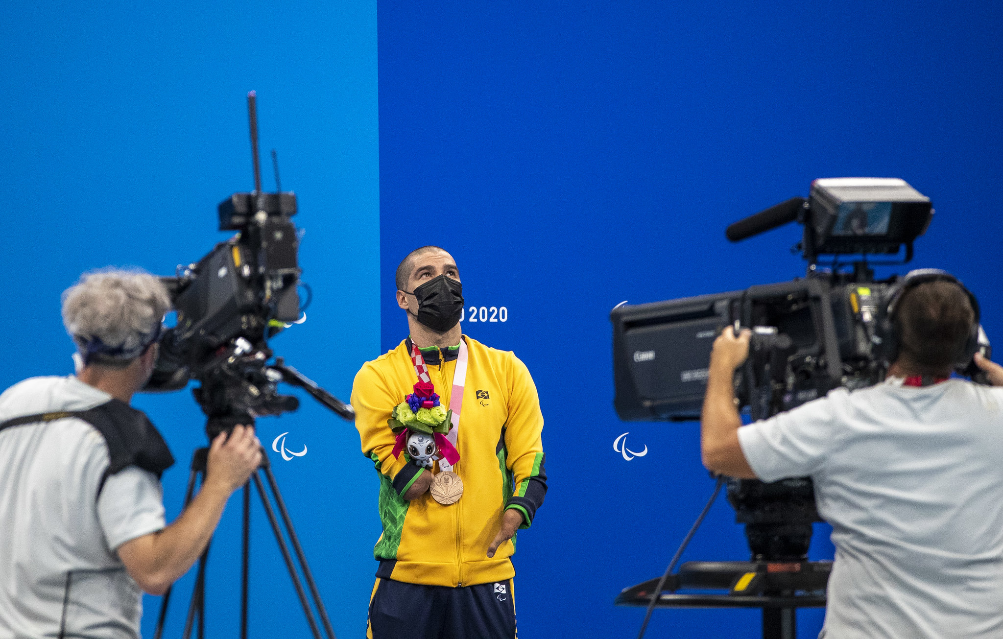 25/08/2021: Nadador paralímpico brasileiro Daniel Dias usa uniforme, máscara facial e uma medalha de bronze no peito enquanto é filmado por duas câmeras nas finais da natação no Tokyo Aquatic Center. Foto: Ale Cabral/CPB. 