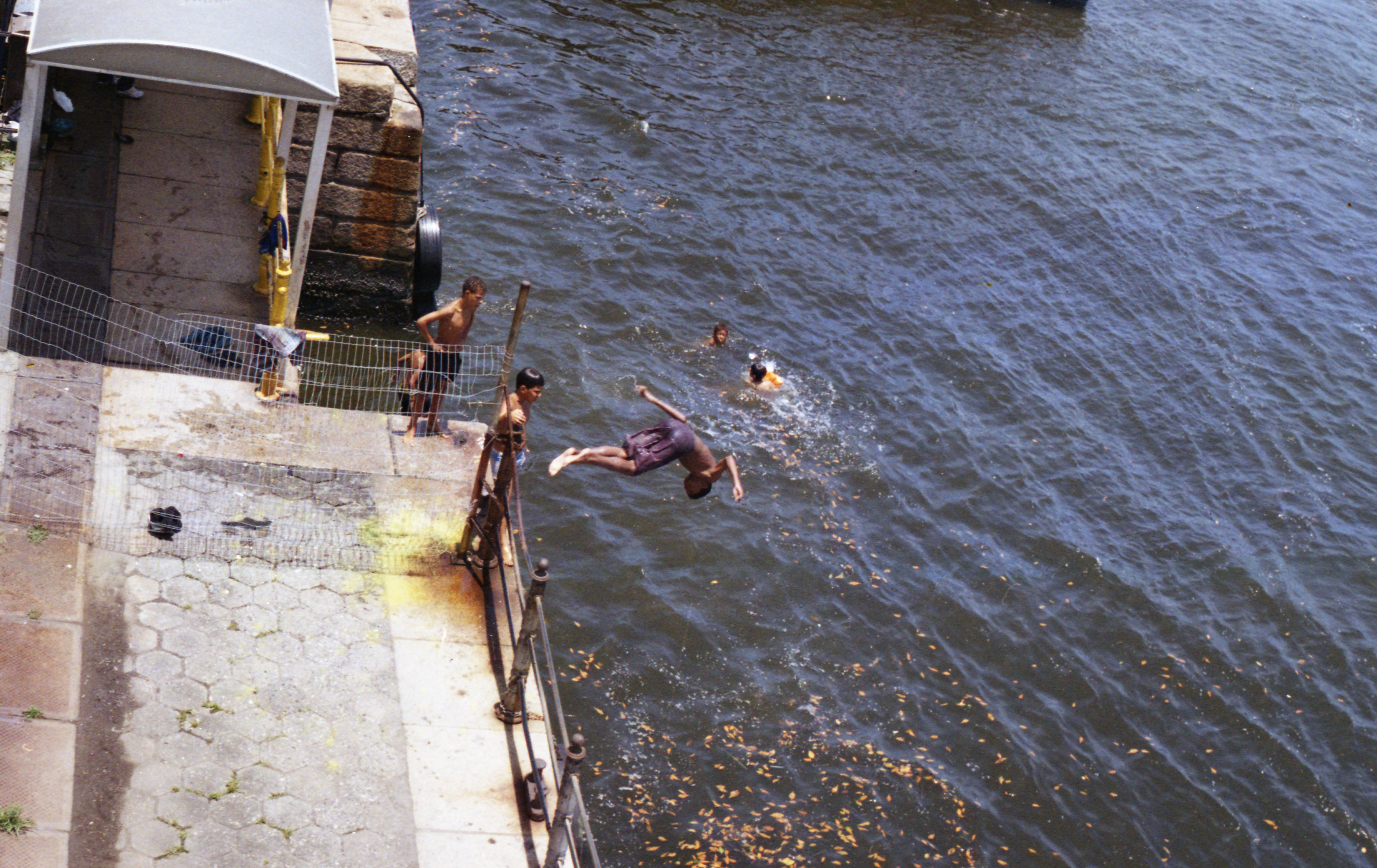crianças pulam de um deck na água.