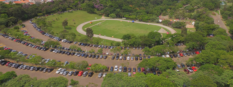 Fotografia aérea mostra os três bolsões de estacionamento do Sesc Interlagos em meio às árvores, com piso de paralelepípedos. Ao fundo está o campo de futebol.