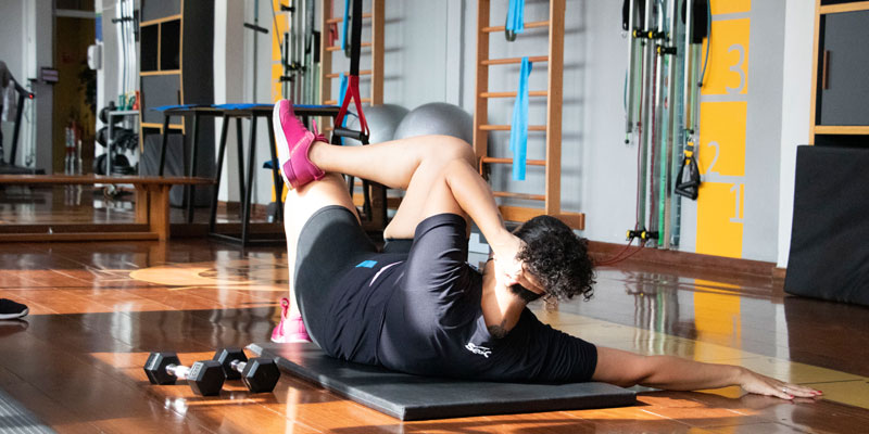 Imagem horizontal de mulher realizando exercício físico de abdominal.