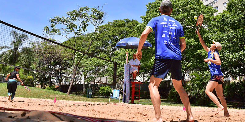 Ao ar livre, duas duplas disputam uma partida de beach tênnis