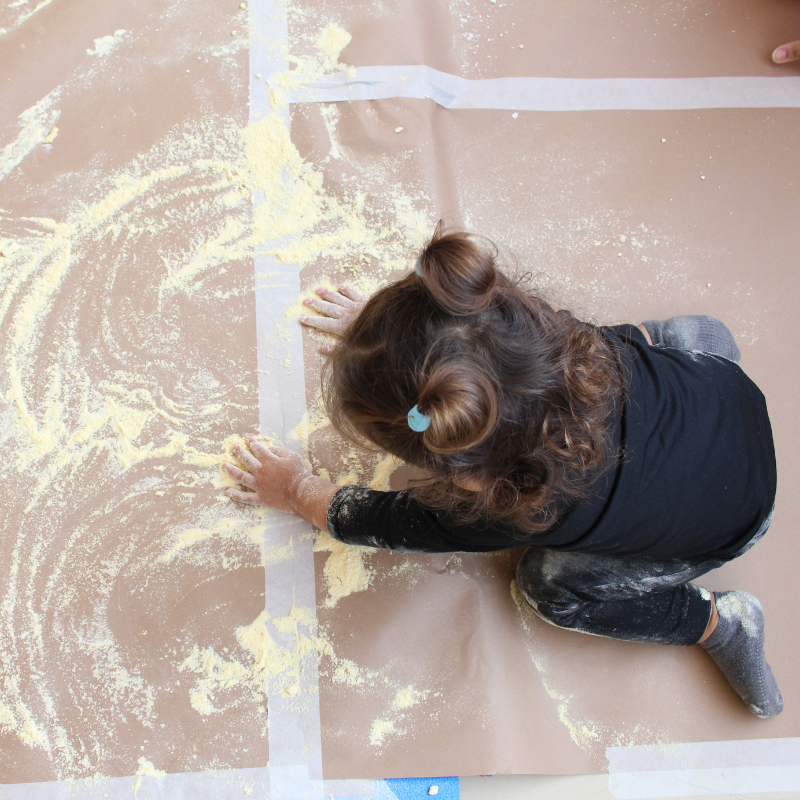 Criança brinca sobre um papel com um pó amarelo. Foto vista de cima.