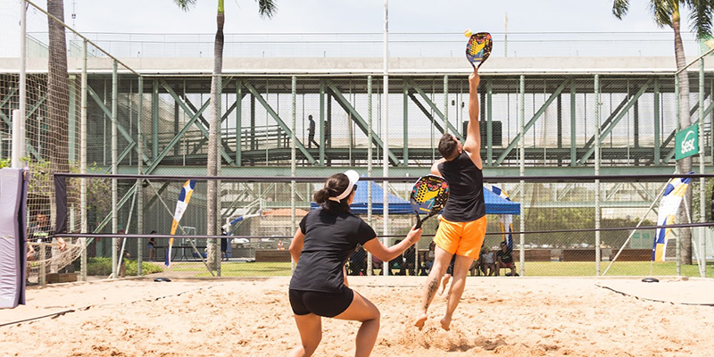 Dois jogadores de beach tennis em ação durante uma partida em uma quadra de areia ao ar livre.