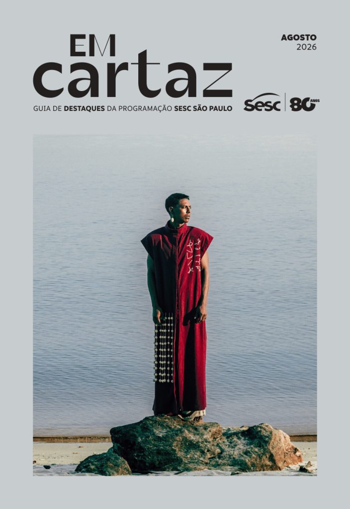 Capa do guia Em Cartaz tem a cor cinza no fundo e, ao centro, a fotografia de um homem indígena, posando tranquilo sobre uma pedra, trajando uma roupa vinho de produção autoral indígena