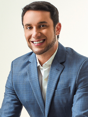 Retrato de Alex Duarte, sorrindo, com camisa azul e fundo neutro.
