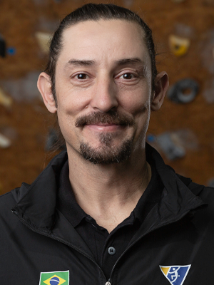 Retrato de Andrew Oliveira, sorrindo, com barba e camisa escura. 